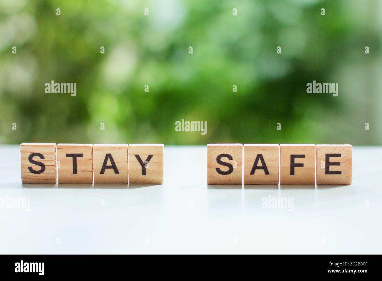 Word stay safe message sign of wooden cubes on a light table against a background of green leaves in soft focus social distancing, concept staying at Stock Photo