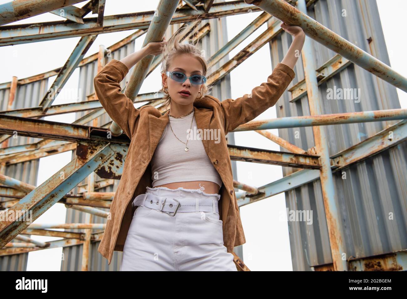 young model in blue sunglasses posing near rusty construction on rooftop Stock Photo