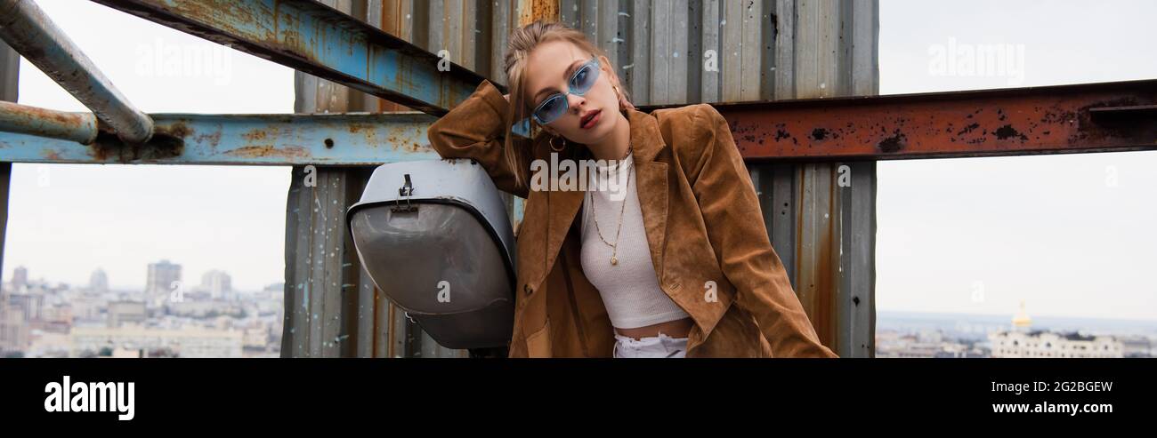 trendy model in blue sunglasses and stylish outfit posing on rusty ...