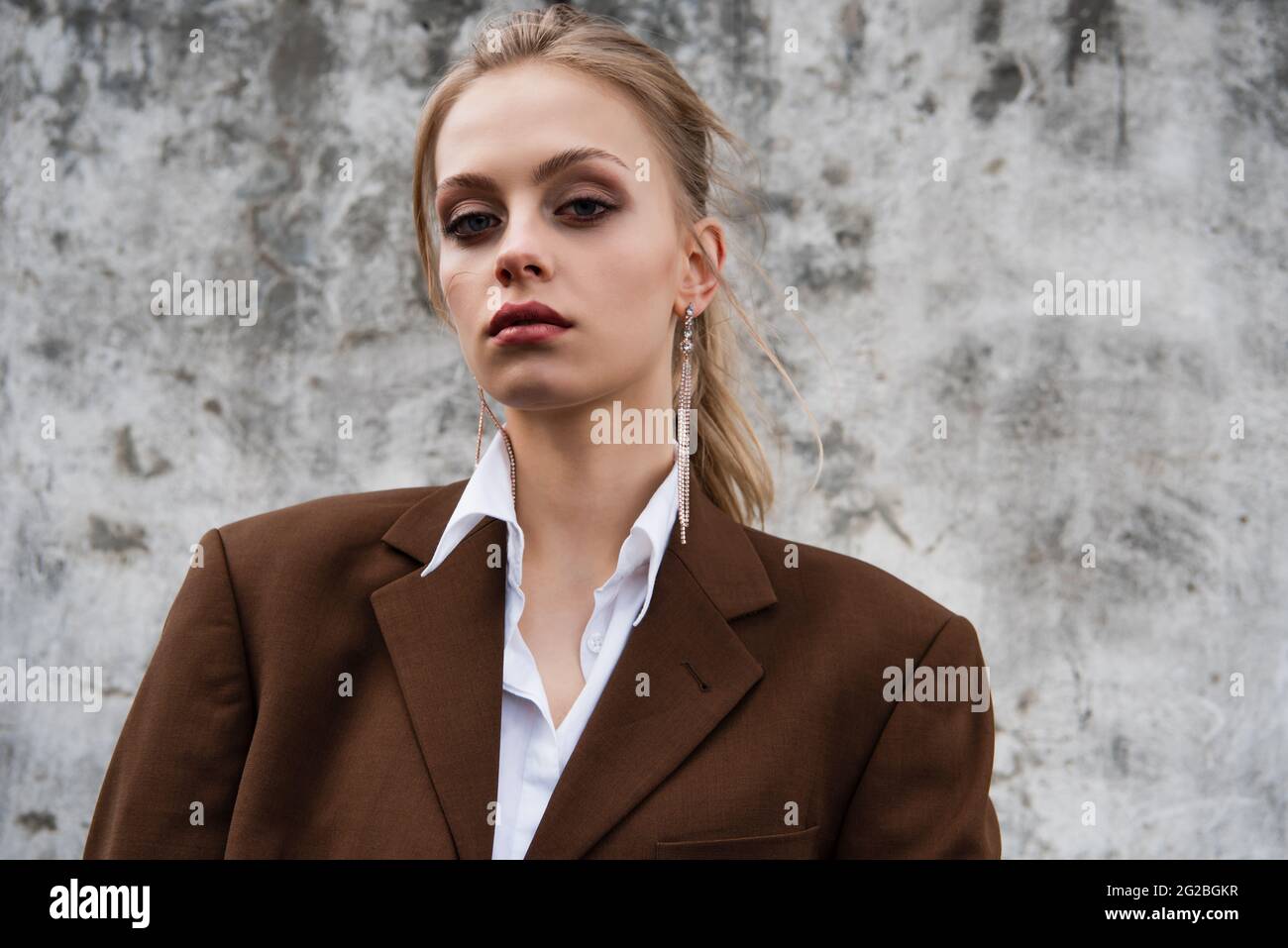 young model in trendy brown blazer posing near concrete wall Stock Photo