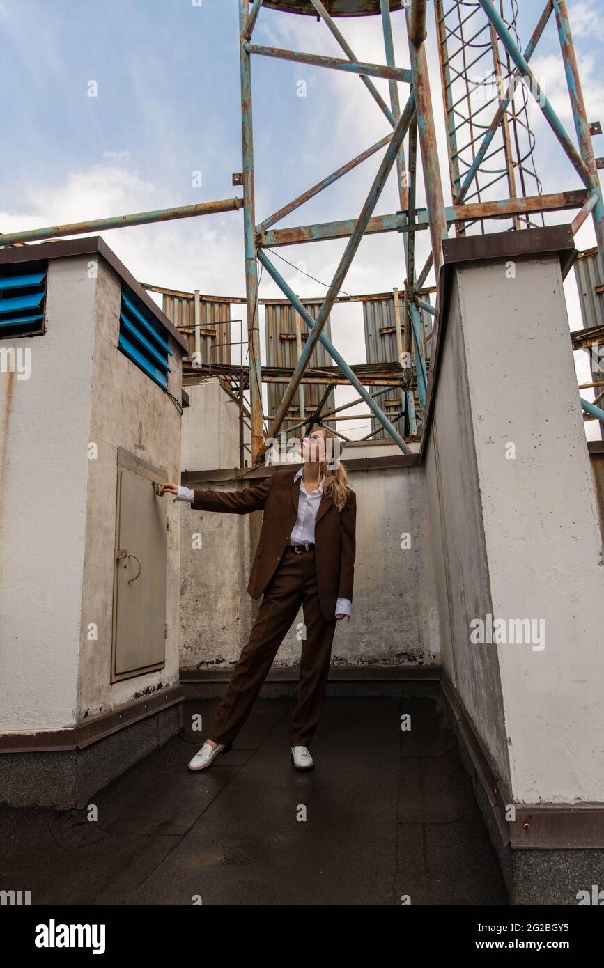 full length of trendy model in sunglasses and brown suit posing on rooftop Stock Photo