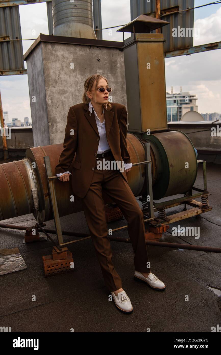 full length of model in sunglasses and trendy brown suit posing on rooftop Stock Photo