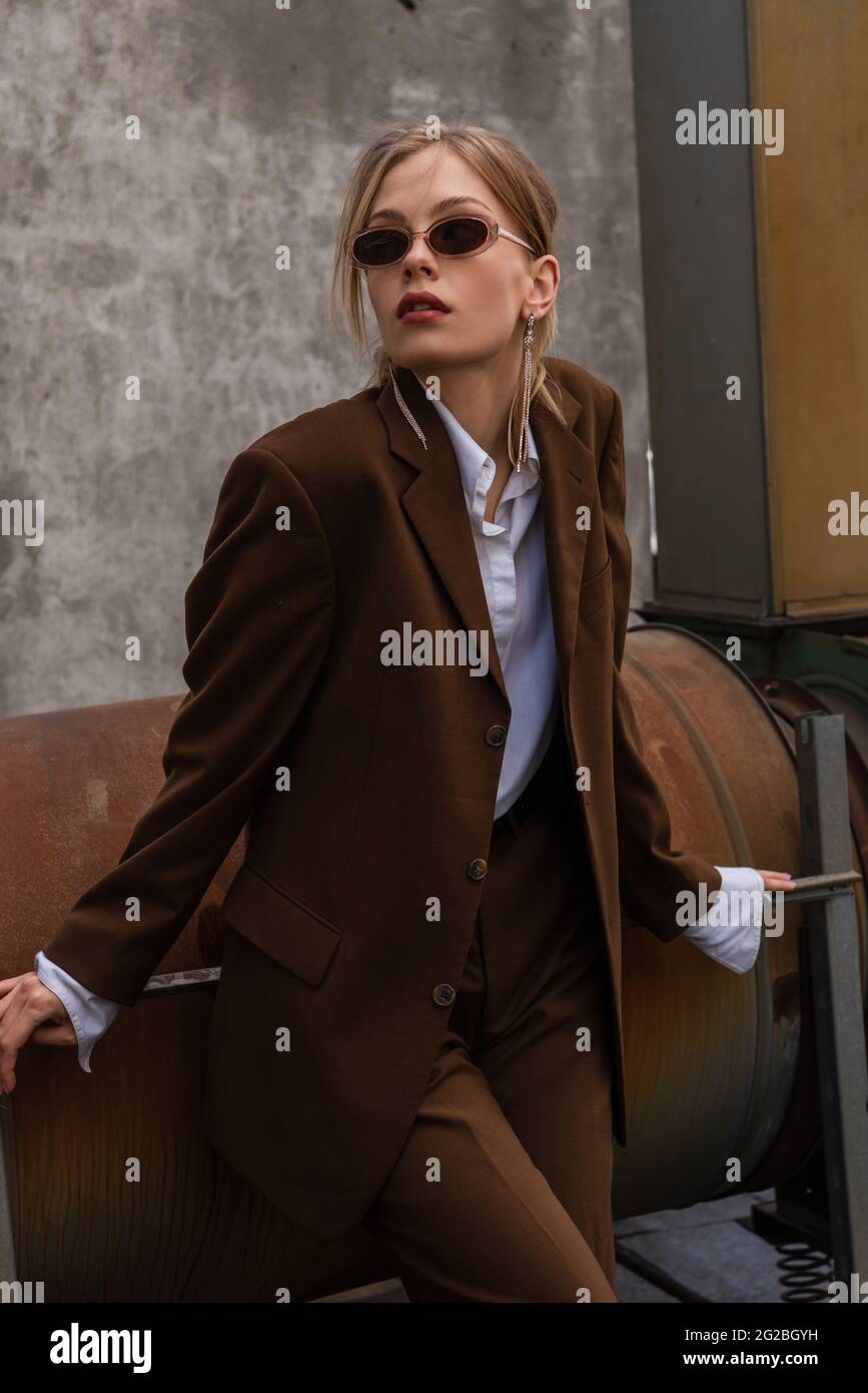 young blonde model in sunglasses and trendy brown suit posing on rooftop Stock Photo