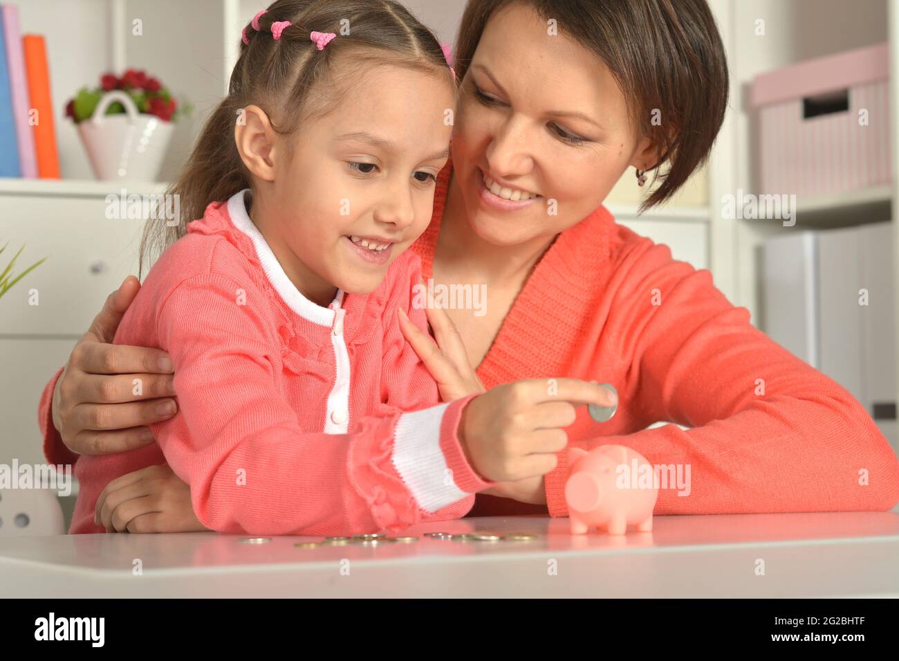 Mother and child daughter putting coins into piggy bank Stock Photo - Alamy