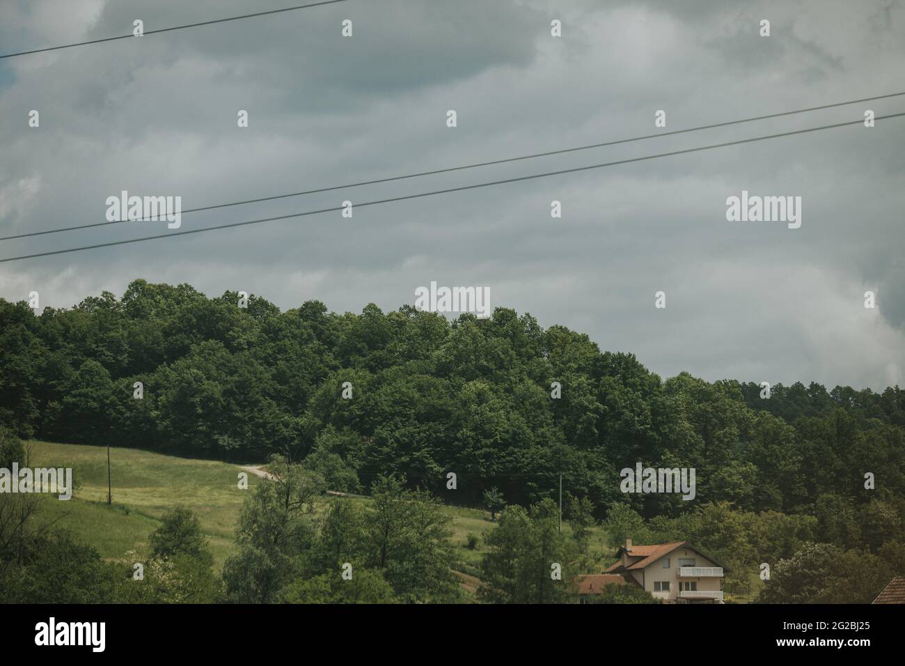 Rural scenery of a house and trees on hills on a cloudy day Stock Photo ...
