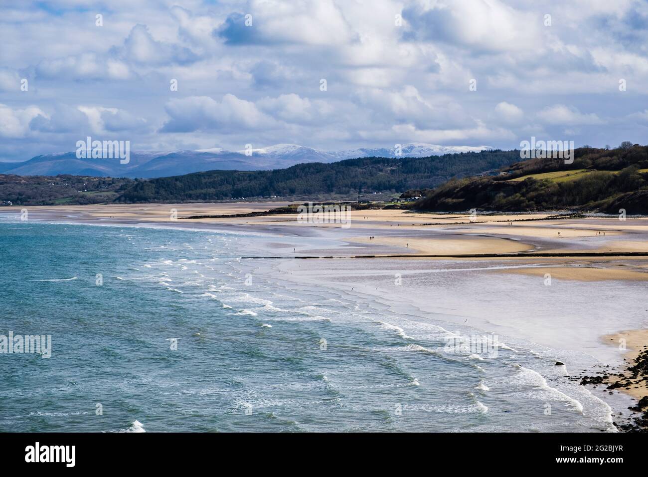 View across quiet sandy beach at low tide to distant snow capped mountains of Snowdonia. Benllech, Isle of Anglesey, Wales, UK, Britain Stock Photo