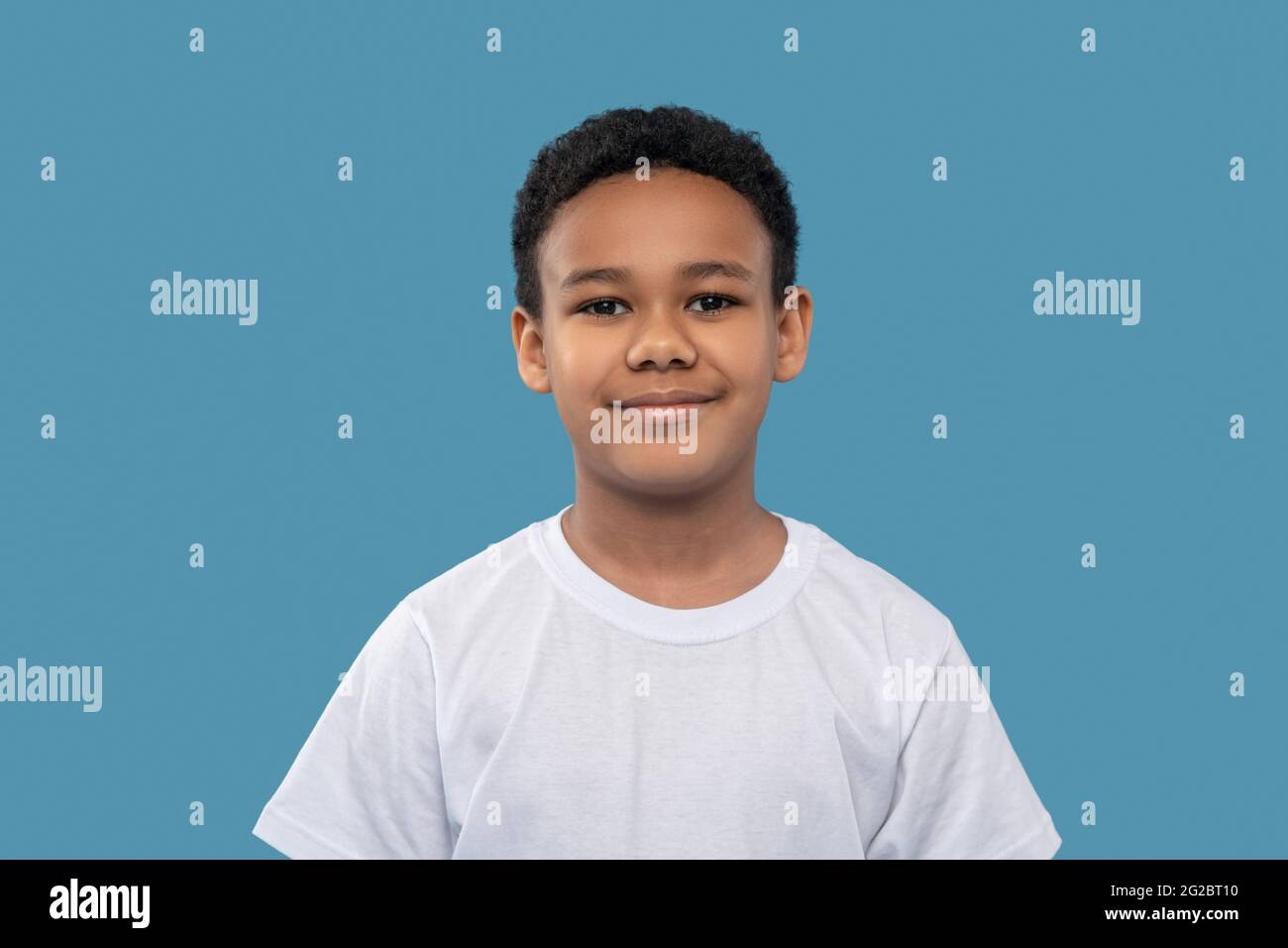 Smiling friendly dark-skinned boy on light blue background Stock Photo