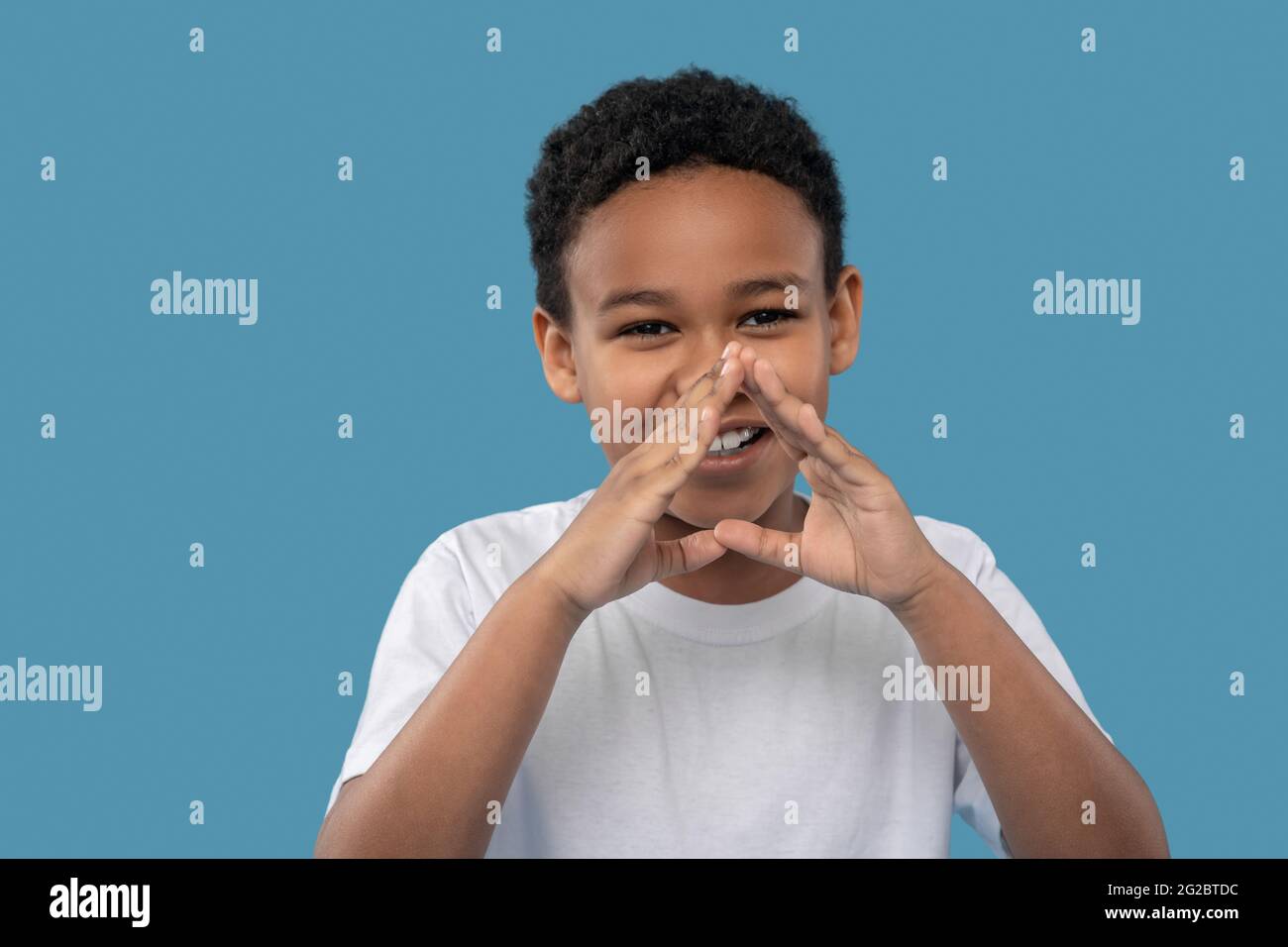 Joyful darkskinned boy holding hands near his mouth Stock Photo