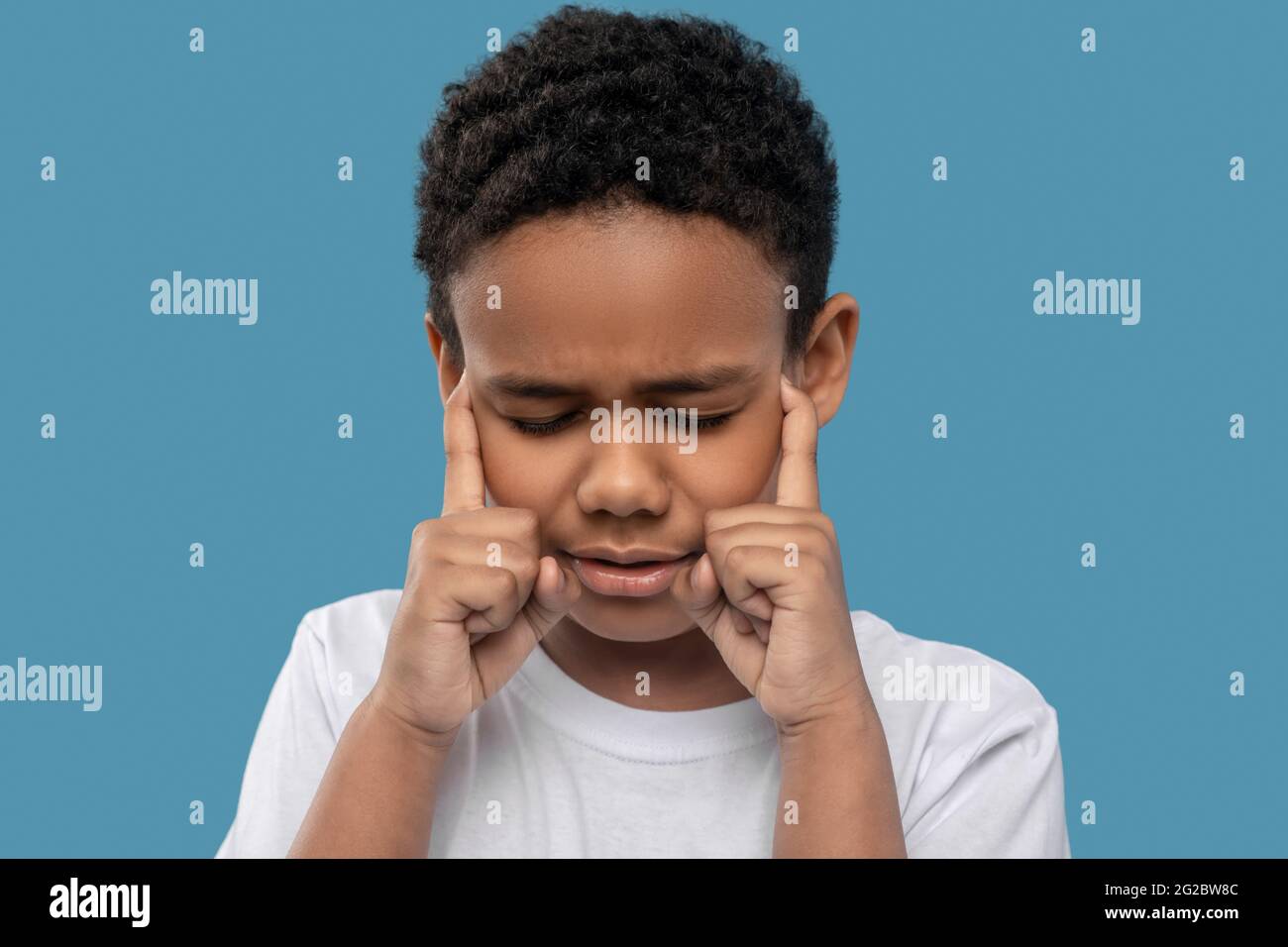 Darkskinned boy with closed eyes and unhappy grimace Stock Photo