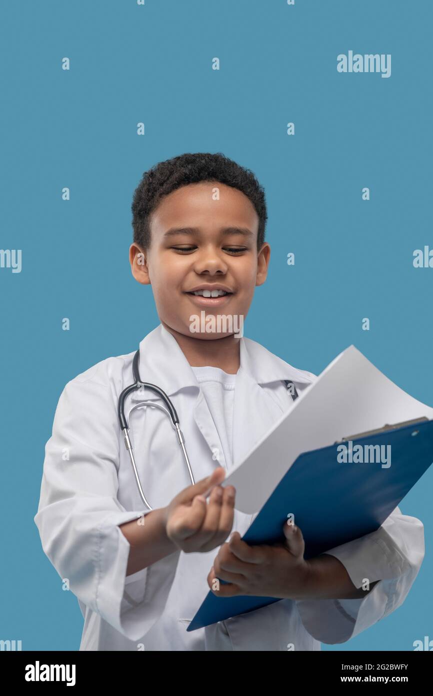 Joyful boy in medical gown looking at paper sheets Stock Photo Alamy