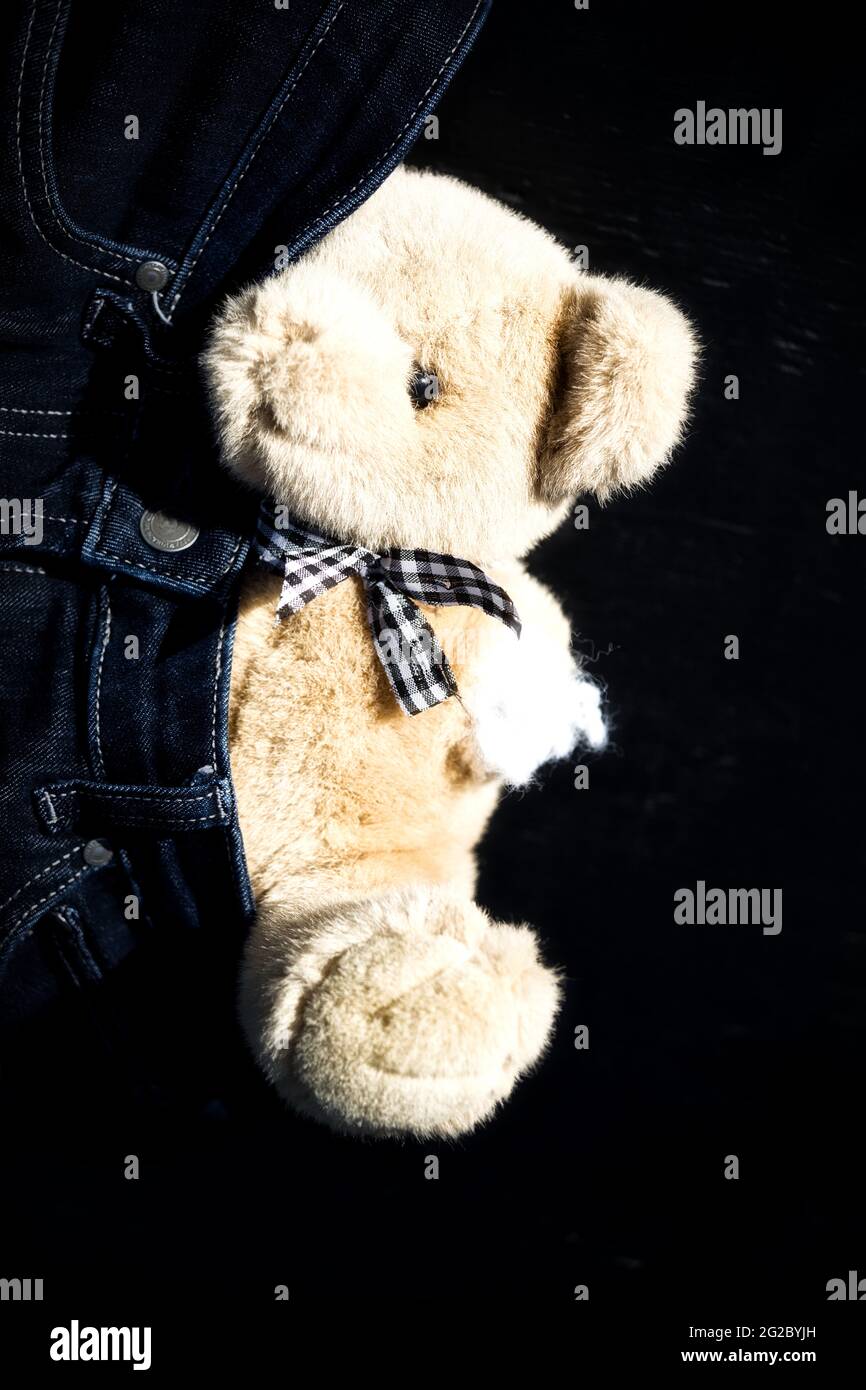 Teddy bear cuddly toy disabled handicapped with amputated missing arm partly hiding in pair of jeans. Concept of equality, non conformity, different Stock Photo