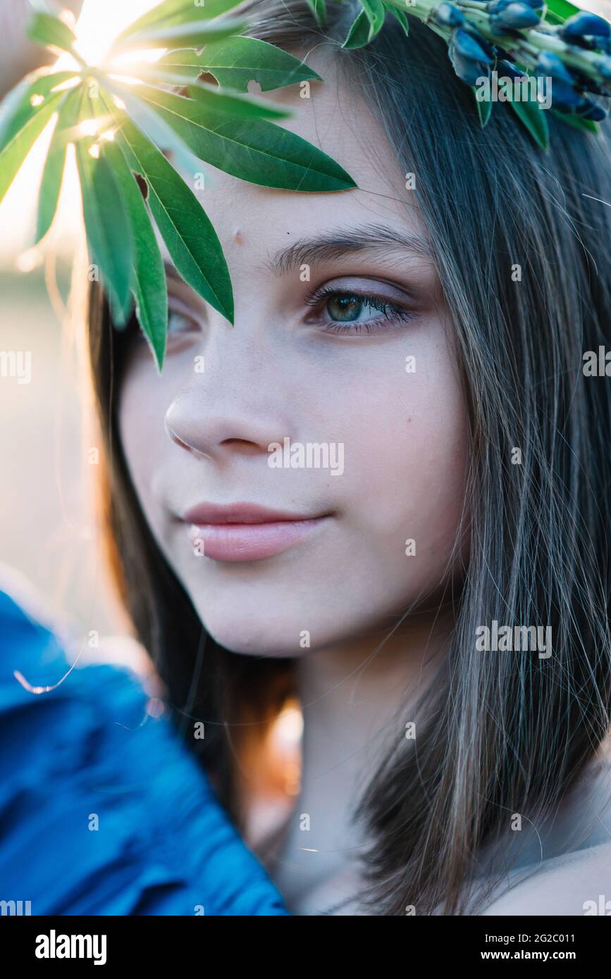 Beautiful girl covers her face with green leaves of a lupine flower. Closeup. Big eyes Stock