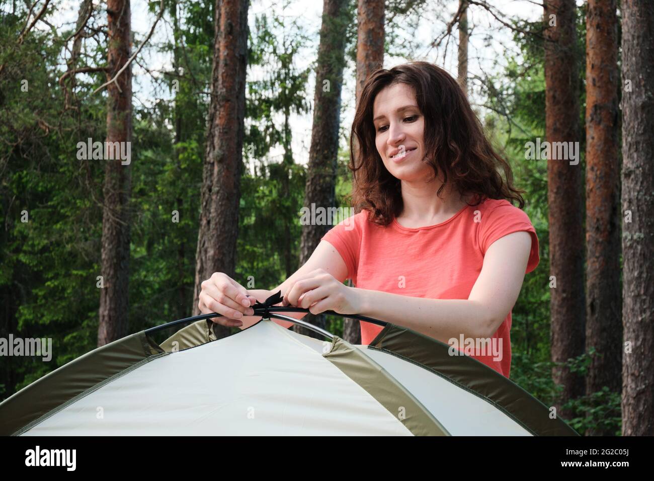 The girl assembles a camping tent. Travel outside the city in the woods. Camping. Stock Photo