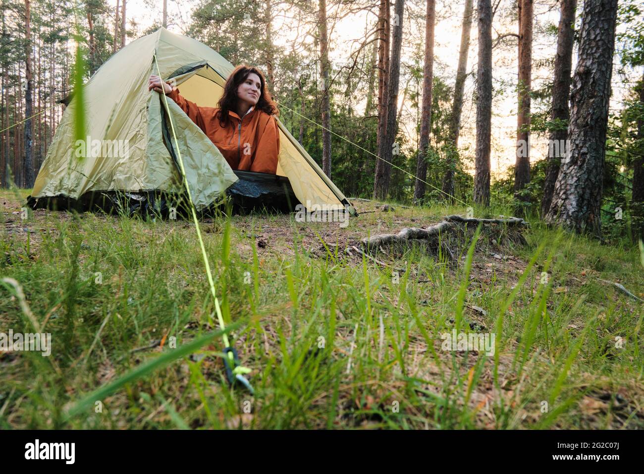 The girl comes out of the tent after sleeping. Travel outside the city in the woods. Camping. Stock Photo