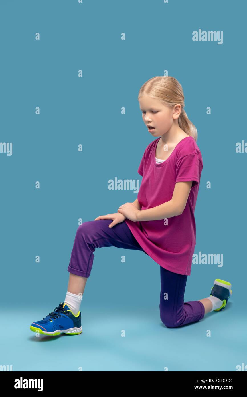 Girl doing exercises standing on one knee on floor Stock Photo