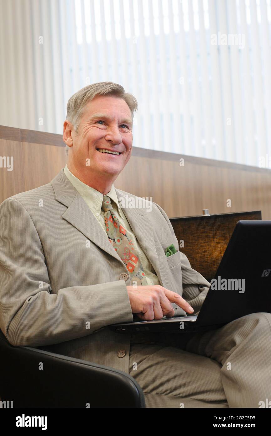 Businessman working at a laptop in a railway station lounge in England. Stock Photo
