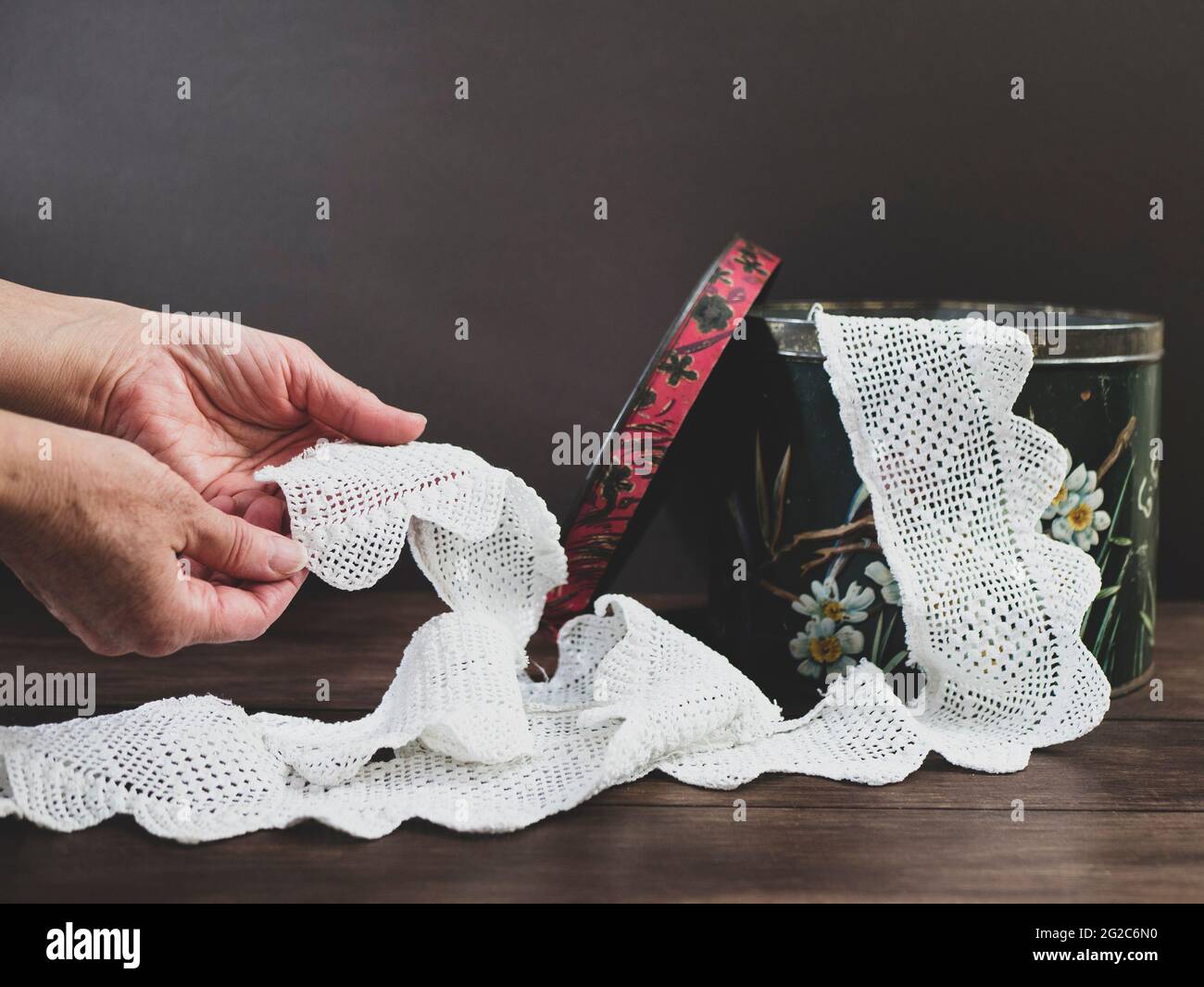 Hands of elderly woman are holding beautiful vintage crisp white lace ribbon. Concept of recollections of youth, nostalgia Stock Photo