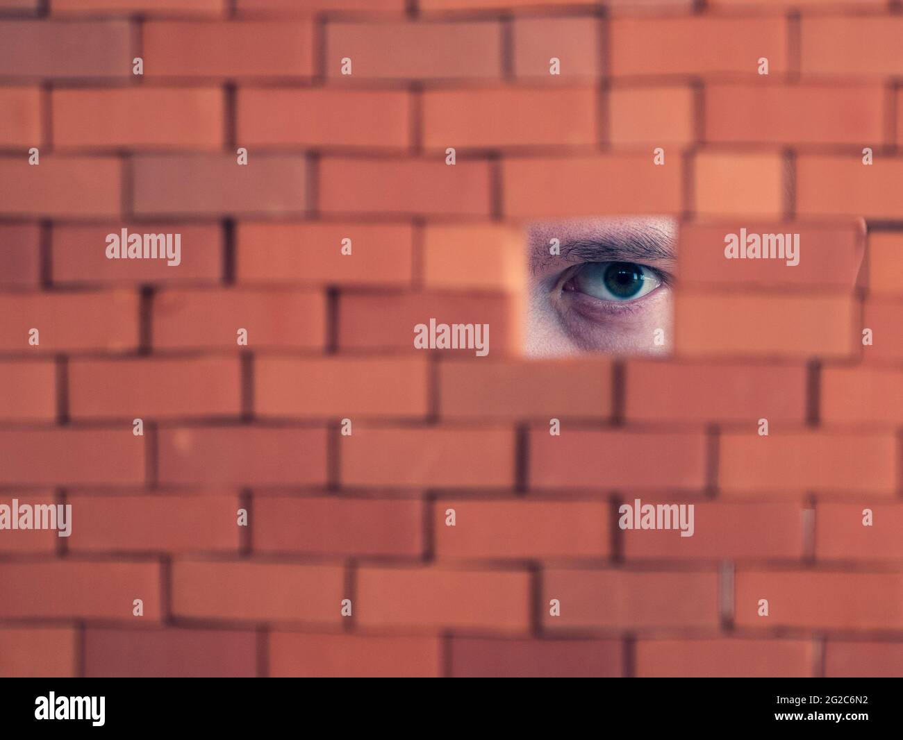 Suspicious person looking through the hole in the brick wall. Concept of spying, haunting and