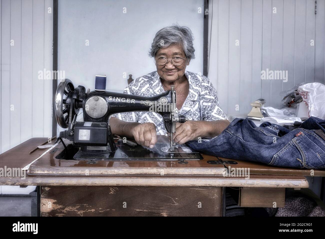 Senior woman working. Seamstress rearing clothes using a vintage singer sewing machine. Thailand Southeast Asia Stock Photo