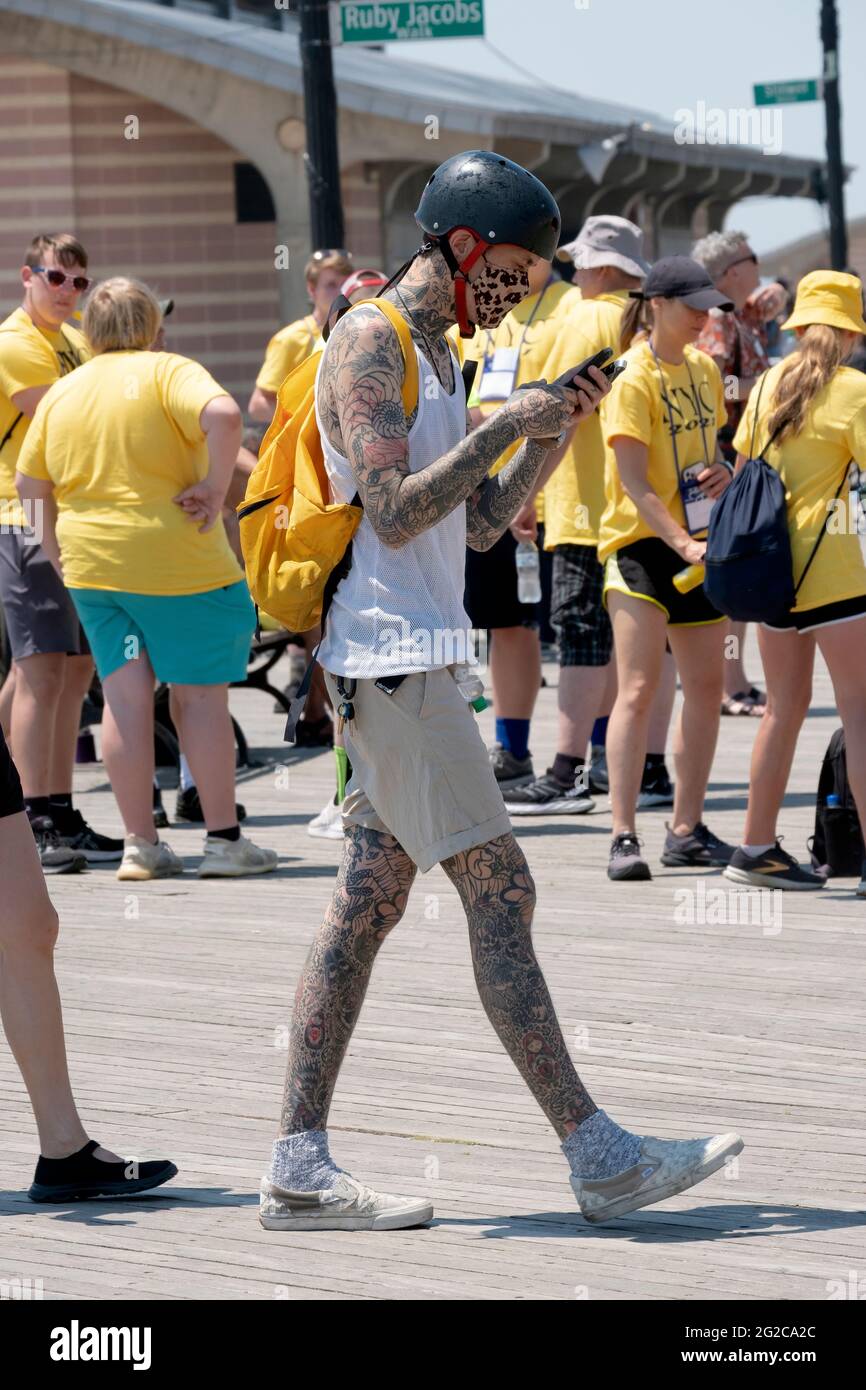 A man with multiple tattoos walks and simultaneously texts on the Coney Island boardwalk in Brooklyn, New York. Stock Photo