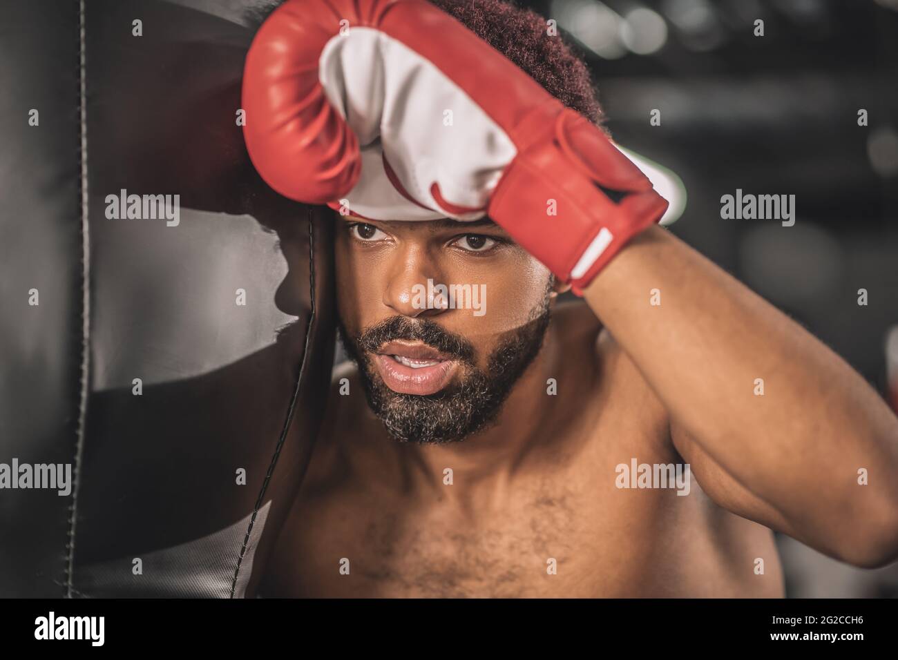 Young dark-skinned kickboxer having a workout in a gym and looking tired Stock Photo