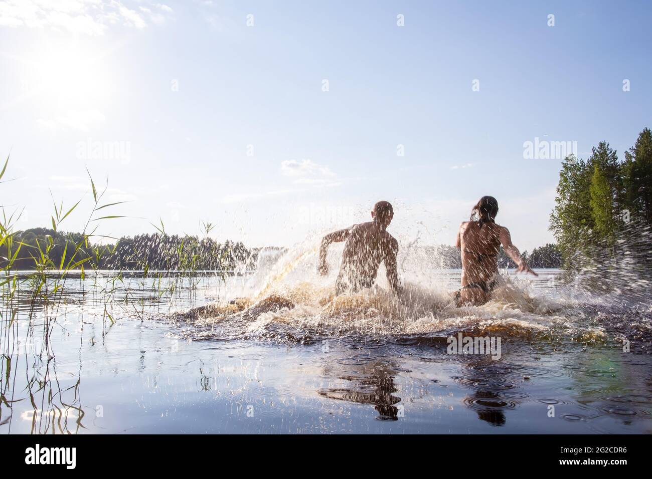 Funny man and woman swim and have fun in a clean forest lake on a hot summer day. Active tourist life. Stock Photo