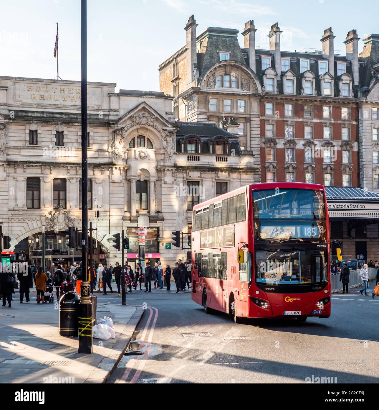 Victoria Railway Station, London. A modern red double decker bus arriving at its marked destination with commuters and the station façade behind. Stock Photo