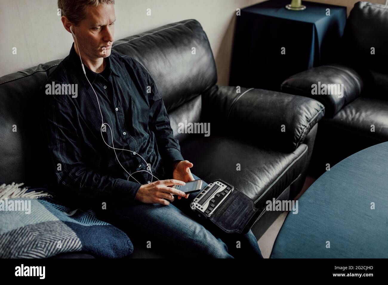 Man sitting on sofa and using Braille keyboard Stock Photo