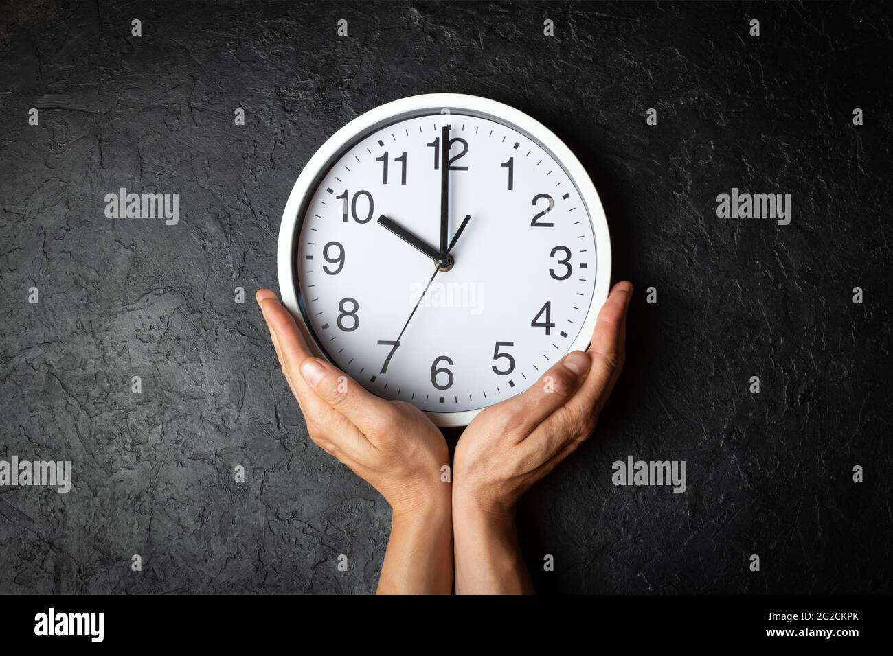 Wall clock on man hands on the black texture background. Flowing time concept Stock Photo