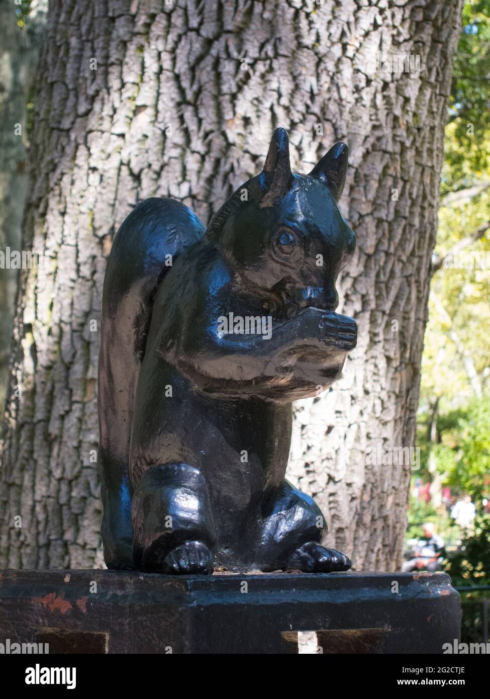 A metal, wrought iron black squirrel sculpture eating an acorn at a park in Brooklyn, New York. Stock Photo