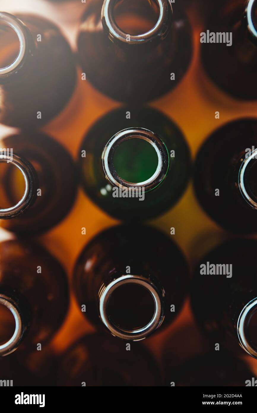 An empty green glass bottle surrounded by other brown bottles seen from above. A beam of light comes from one corner of the image. Stock Photo