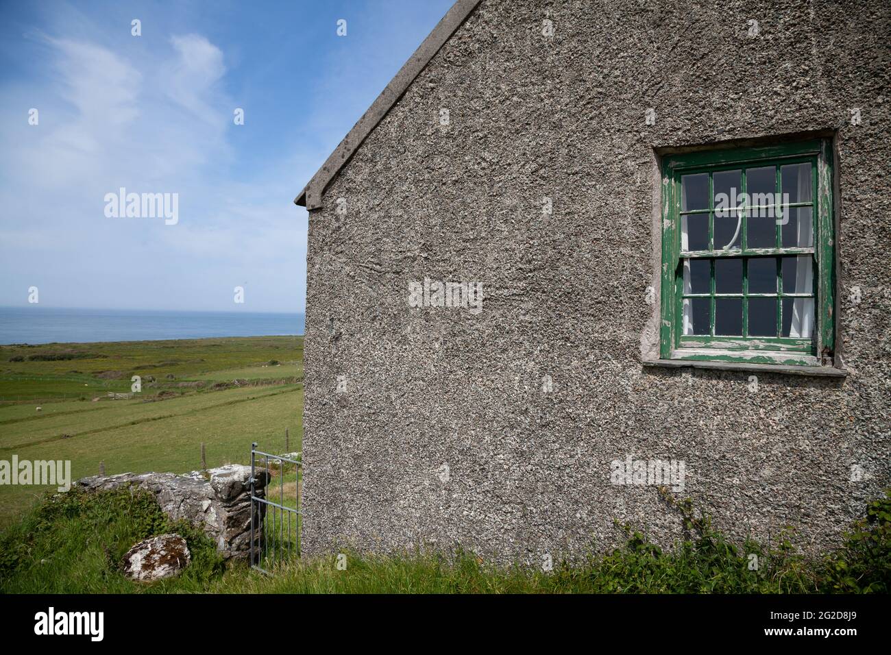 The gable end of the former schoolhouse on Ynys Enlli / Bardsey Island taken on a sunny day with victorian sash window with flaking green paint Stock Photo