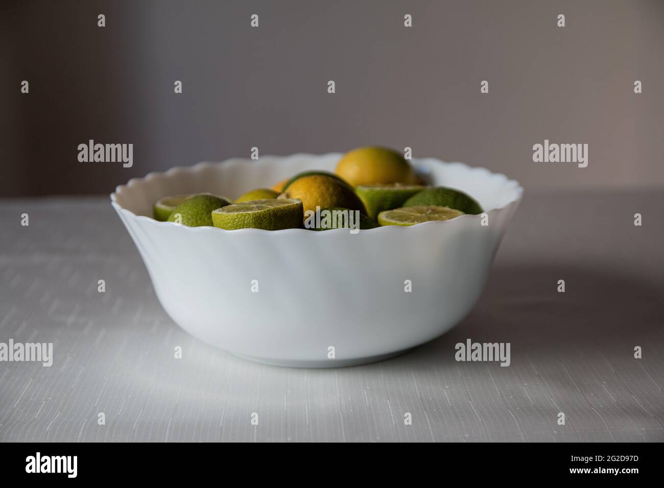 Green limes and yellow lemons inside the white bowl, whole and sliced lemon, citrus Stock Photo