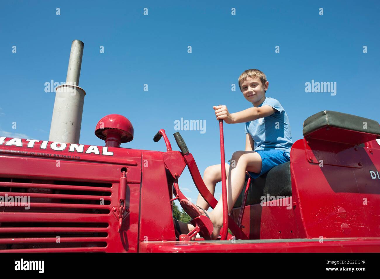 A young boy sits on a bright red vintage restored agricultural tractor