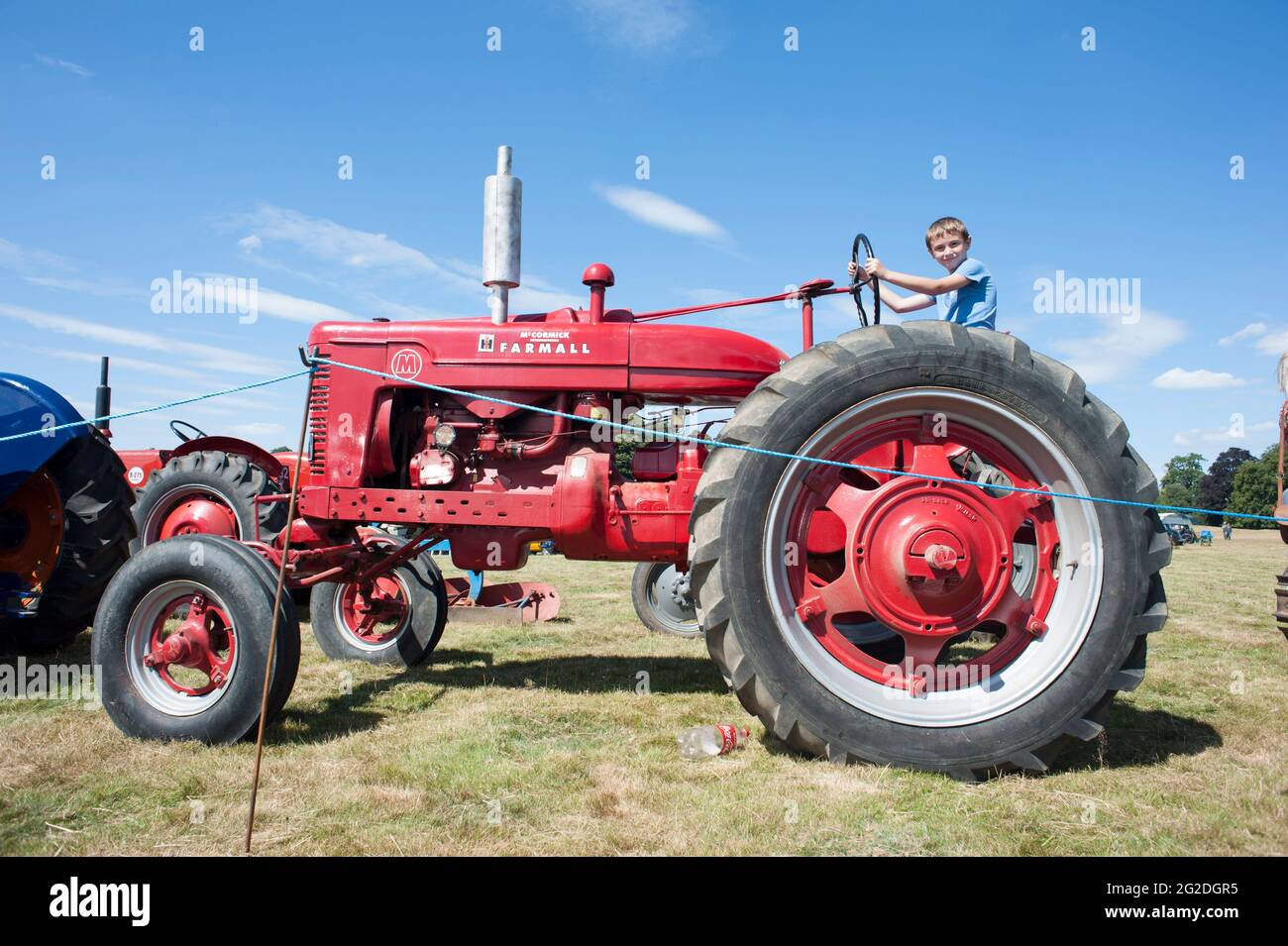 A young boy sits on a bright red vintage restored agricultural tractor