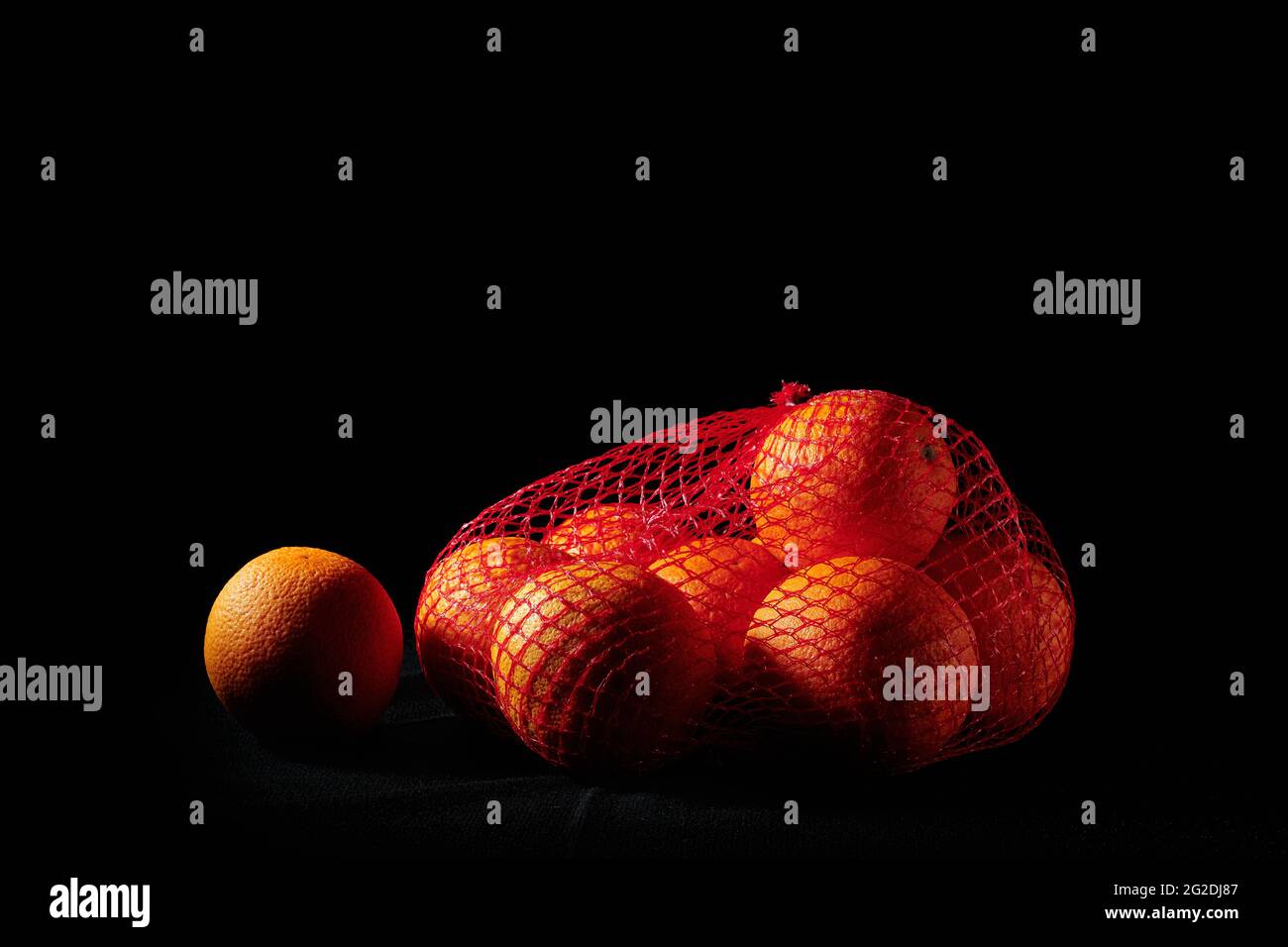 Ripe oranges in a mesh bag on a black background. Stock Photo