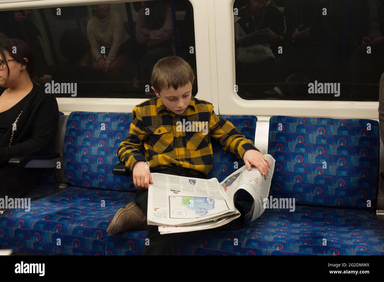 A boy sits on a london underground train and reads the paper. Stock Photo
