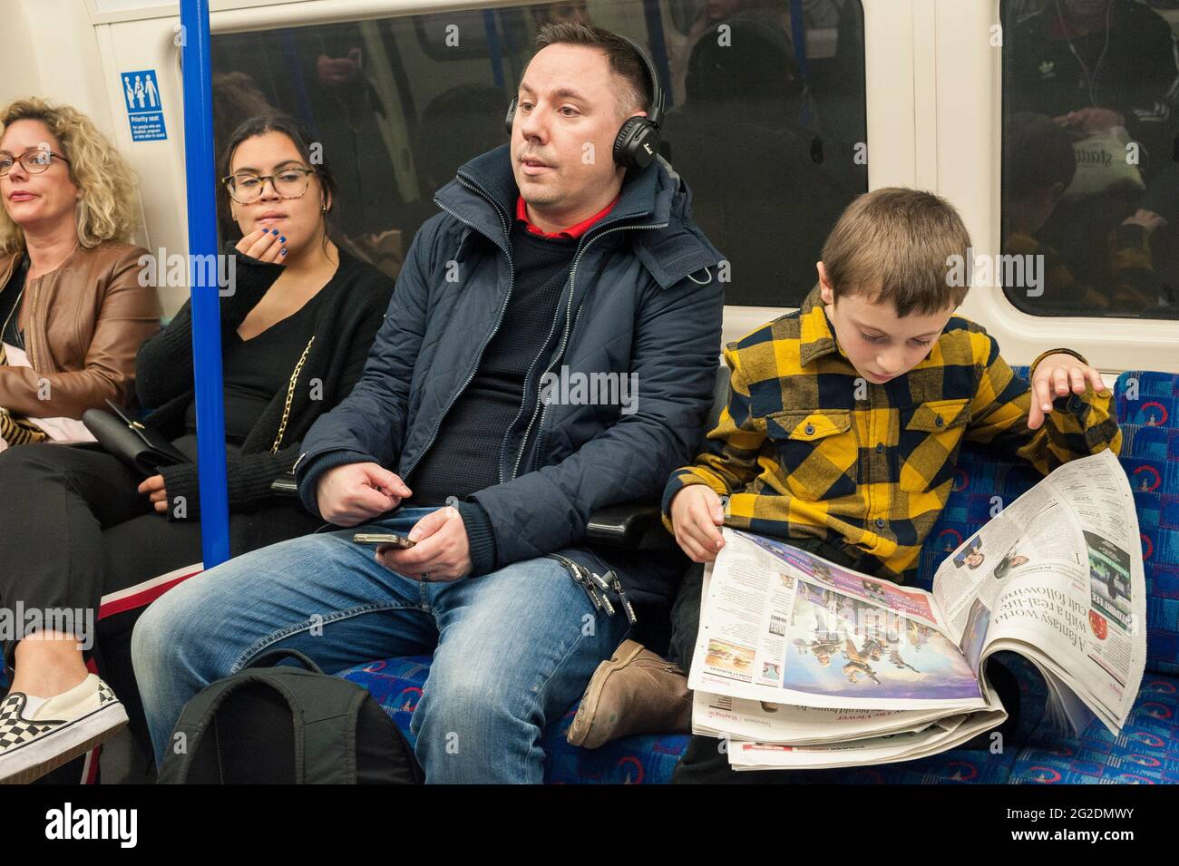 A boy sits on a london underground train and reads the paper. Stock Photo