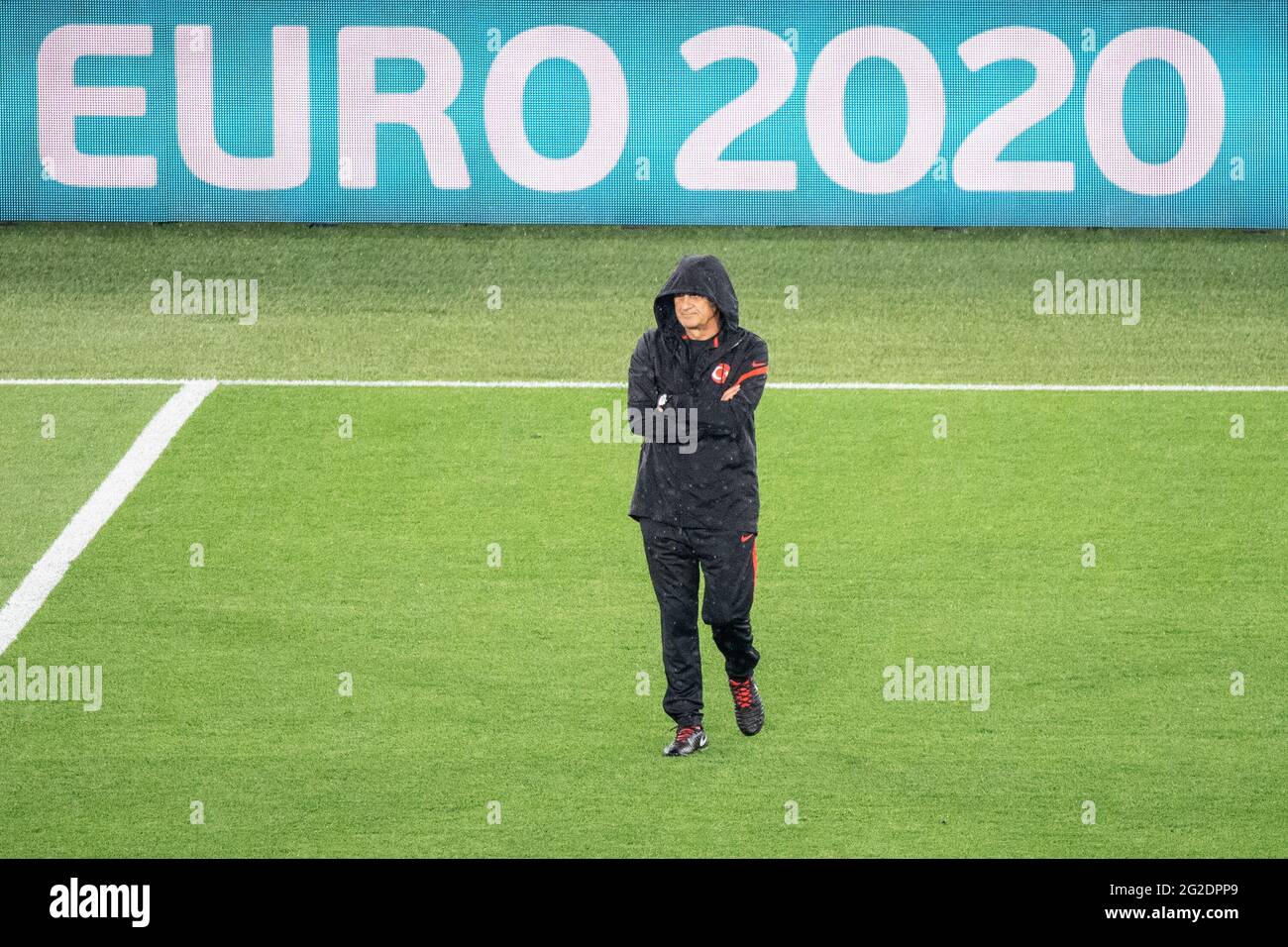 Rom, Italy. 10th June, 2021. Football: European Championship, Turkey national team, training at the Olympic Stadium in Rome. Coach Senol Günes of Turkey is watching the training session and has pulled his hood deep into his face in the rain. In the background, the words 'EURO 2020' can be seen on a digital board. Credit: Matthias Balk/dpa/Alamy Live News Stock Photo