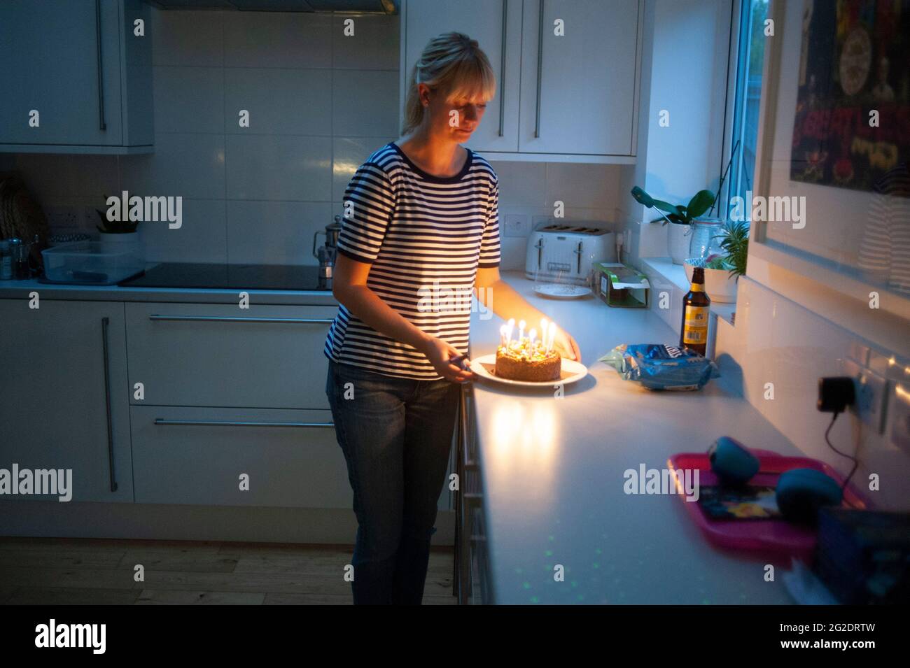 A mother carries a birthday cake after lighting the candles in her kitchen Stock Photo Alamy