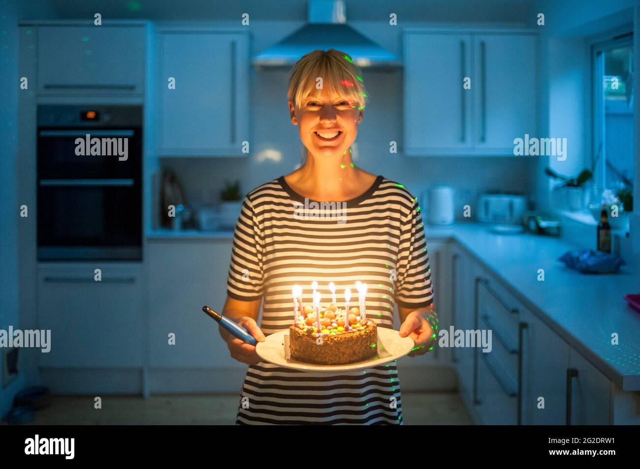 A mother carries a birthday cake after lighting the candles in her kitchen Stock Photo