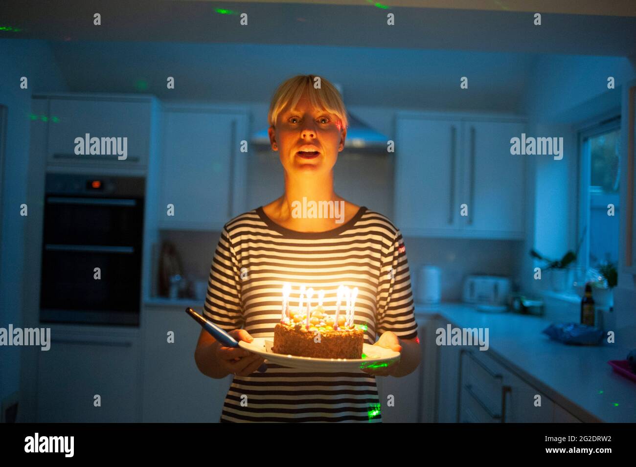A mother carries a birthday cake after lighting the candles in her kitchen Stock Photo Alamy