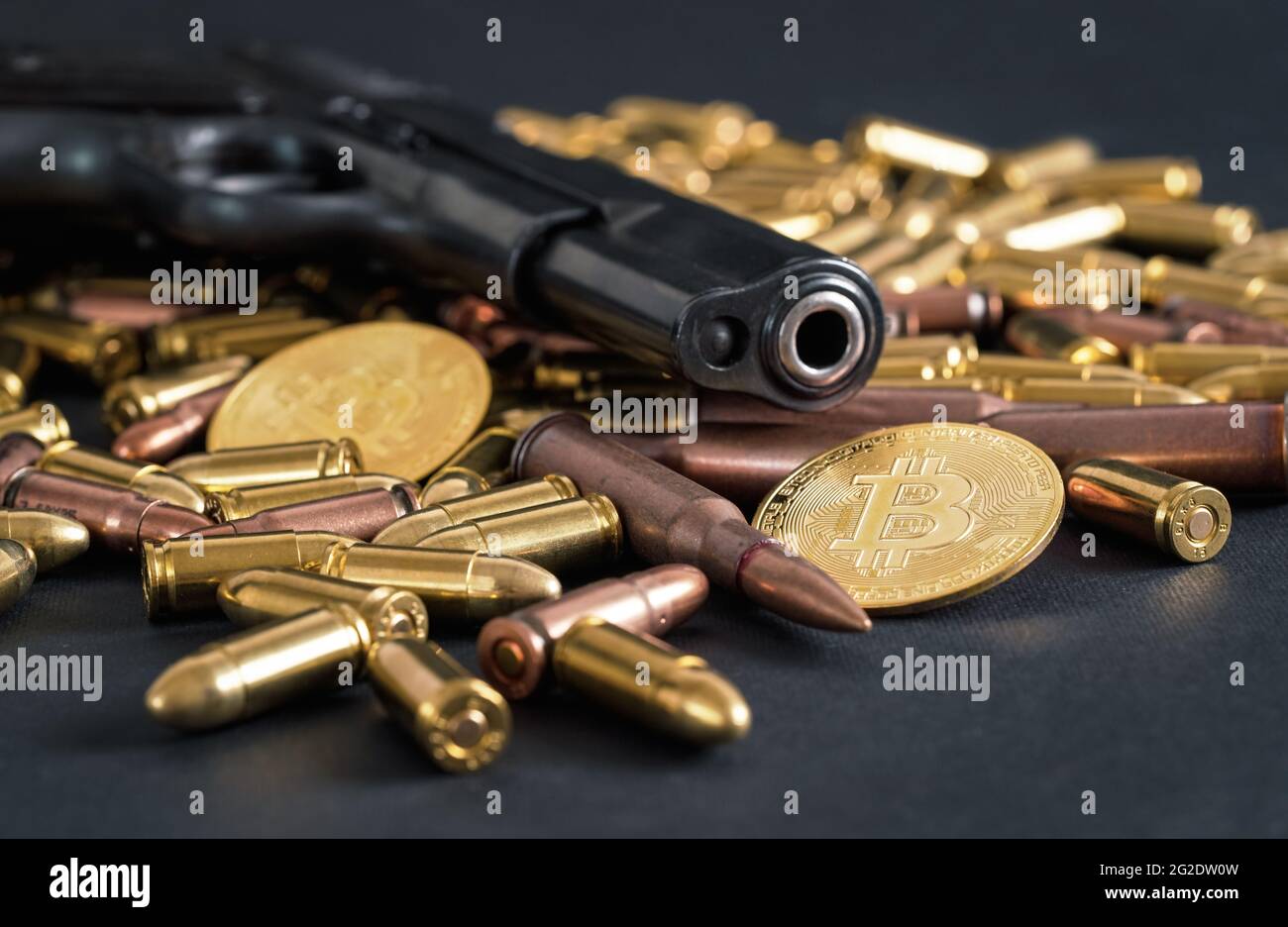 Bronze and brass gun bullets scattered on dark table, black pistol barrel, golden bitcoin coins