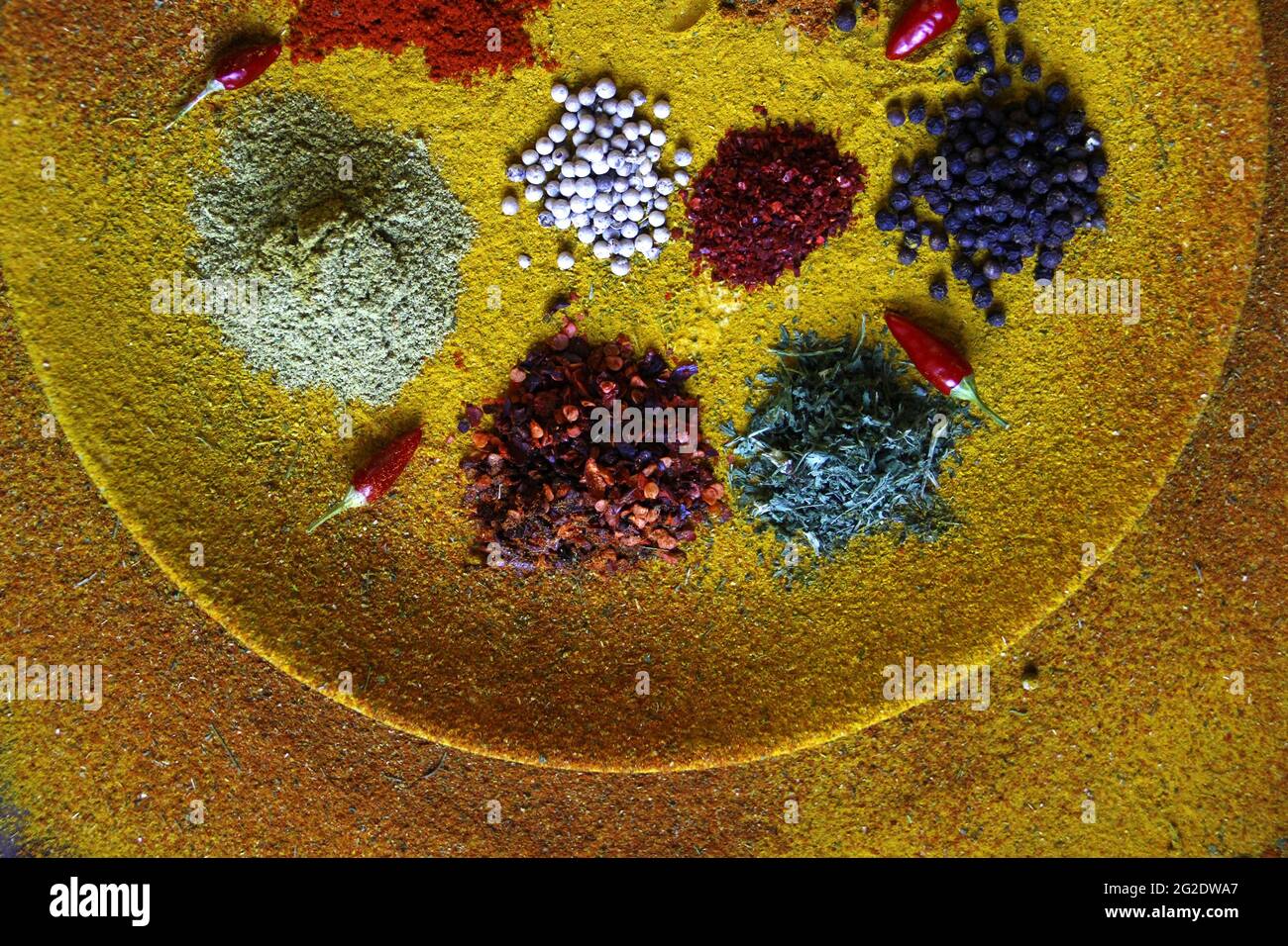 Top view of different condiments and small red chilies on a plate covered with yellow spice Stock Photo