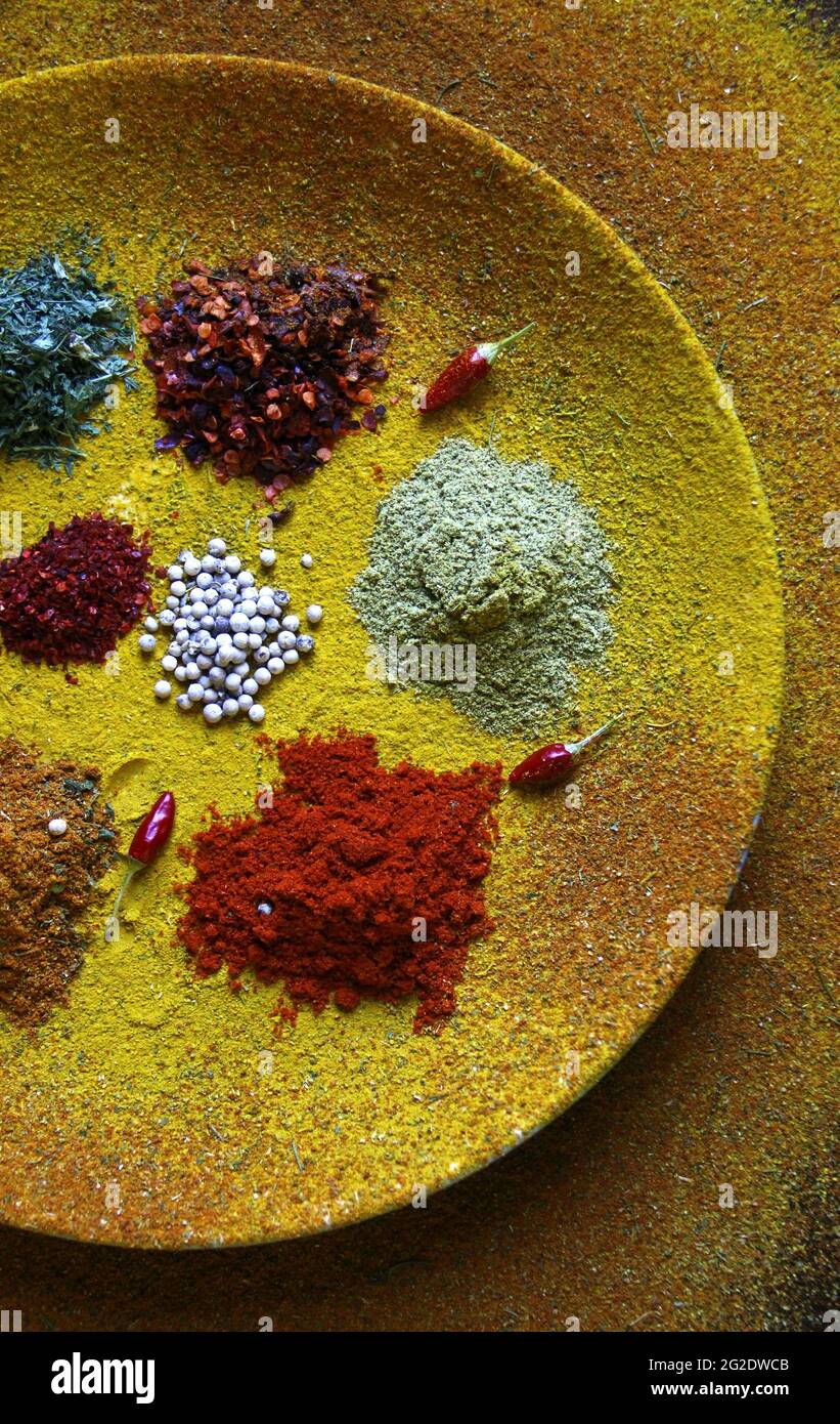 Top view of different condiments and small red chilies on a plate covered with yellow spice Stock Photo