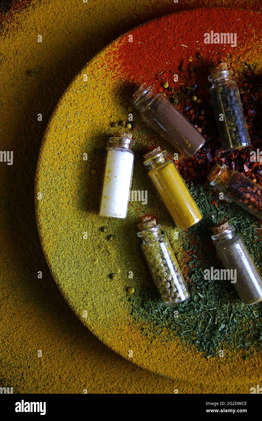 Top view of small bottles filled with various condiments on a plate covered with colorful spices Stock Photo