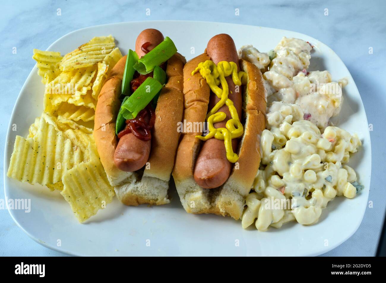 two hot dogs with macaroni and potato salad with chips on the side