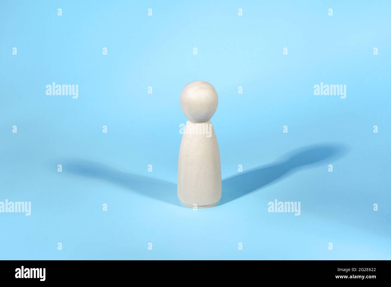 Wooden figure with two shadows on blue backdrop. Abstract concept of lonely person. Stock Photo