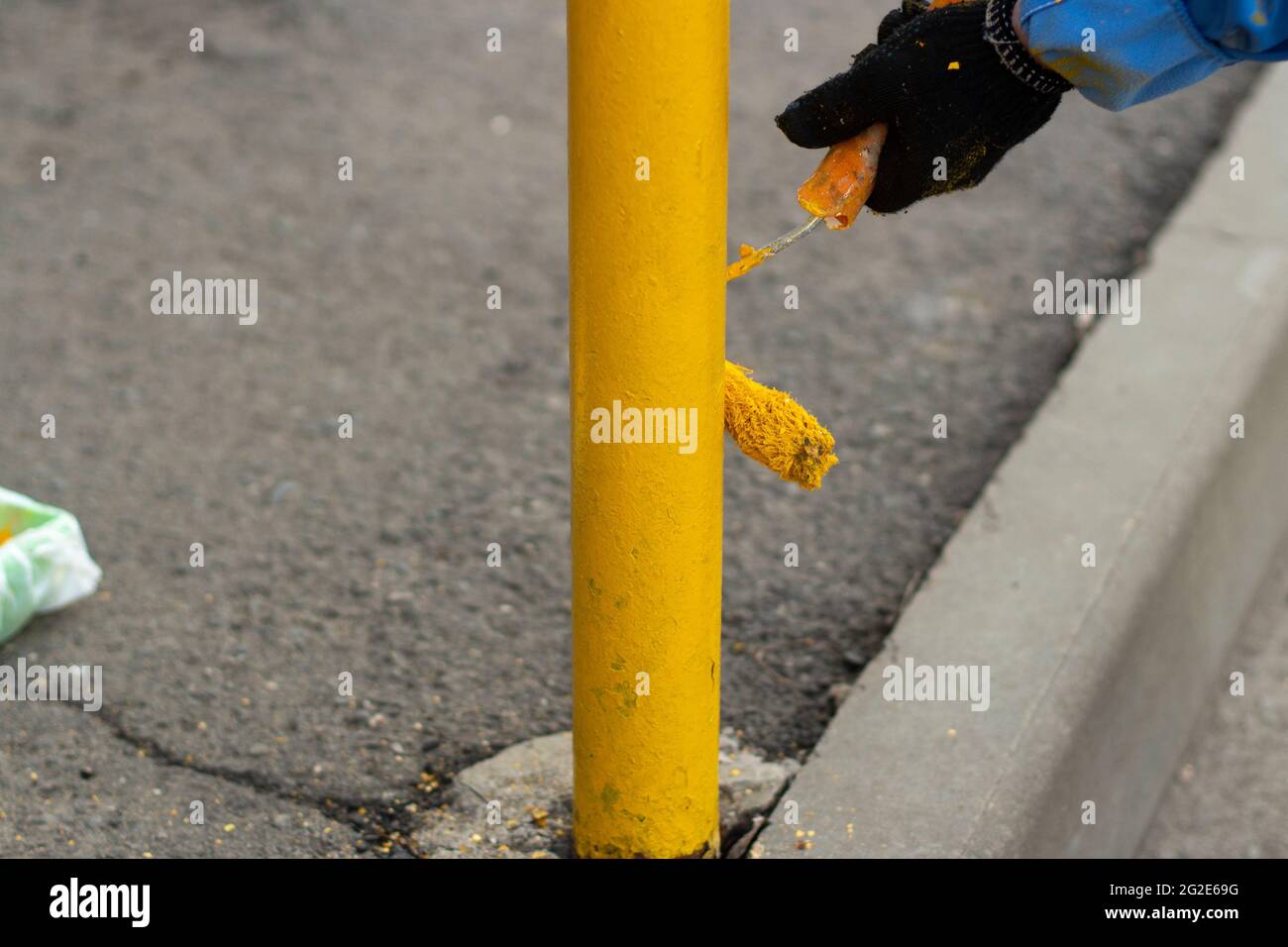 Painting a metal post with yellow paint. Parking bollard painting