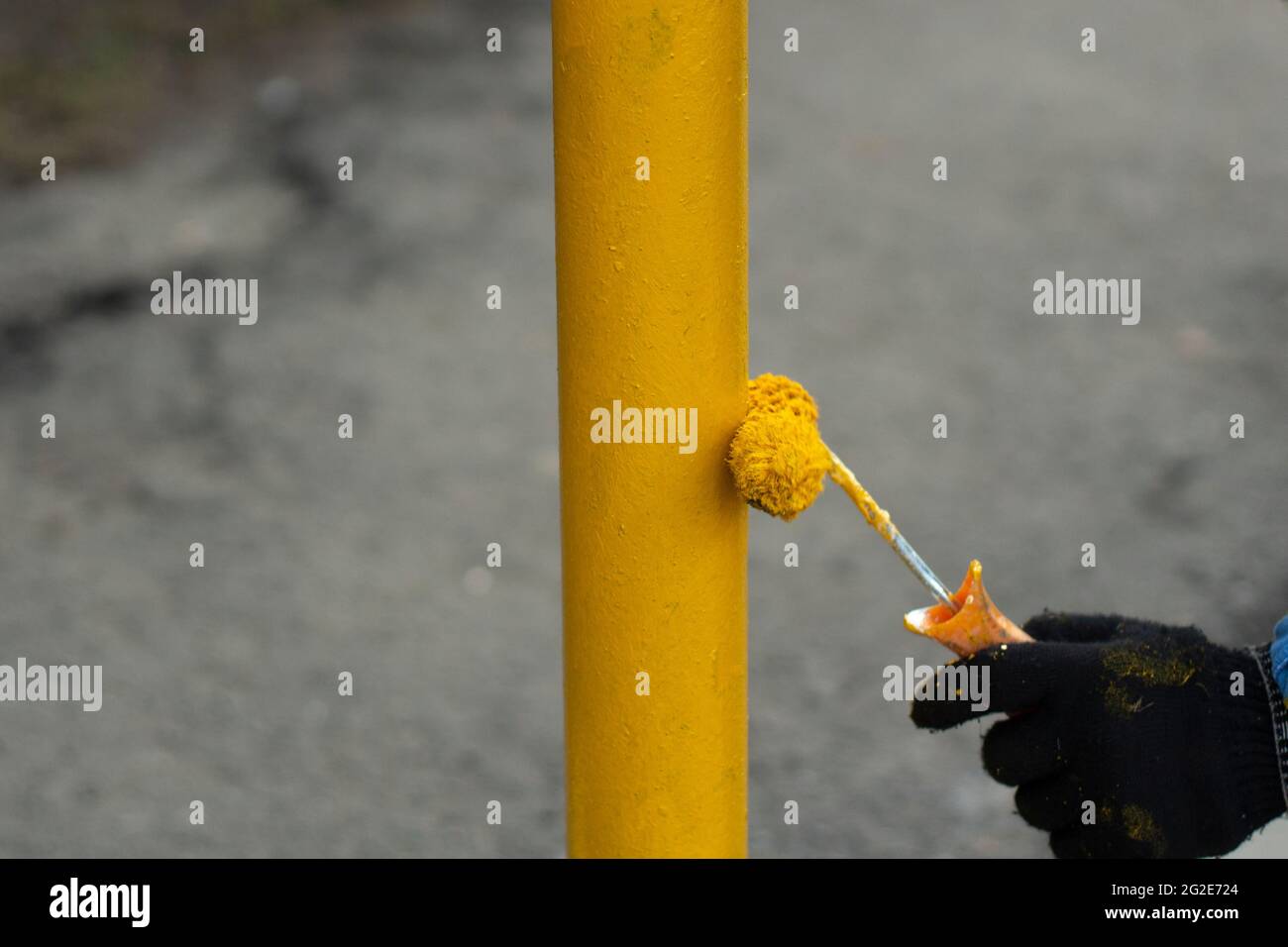 Painting a metal post with yellow paint. Parking bollard painting. Paints with a roller with